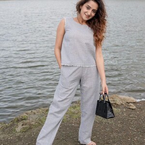 Könnte beinhalten: Ein ärmelloses graues Leinenoberteil und eine passende Hose mit ausgefransten Kanten. Das Outfit wird mit schwarzen Sandalen und einer kleinen schwarzen Handtasche kombiniert. Das Ensemble ist lässig und für warmes Wetter geeignet.