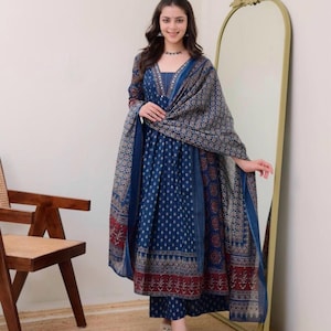 K&ouml;nnte beinhalten: Ein blaues bedrucktes Salwar Kameez-Set mit passendem Dupatta. Das Outfit hat einen V-Ausschnitt und lange &Auml;rmel. Der Stoff hat ein Muster aus kleinen wei&szlig;en Punkten und floralen Bord&uuml;ren. Die Person tr&auml;gt Sandalen.