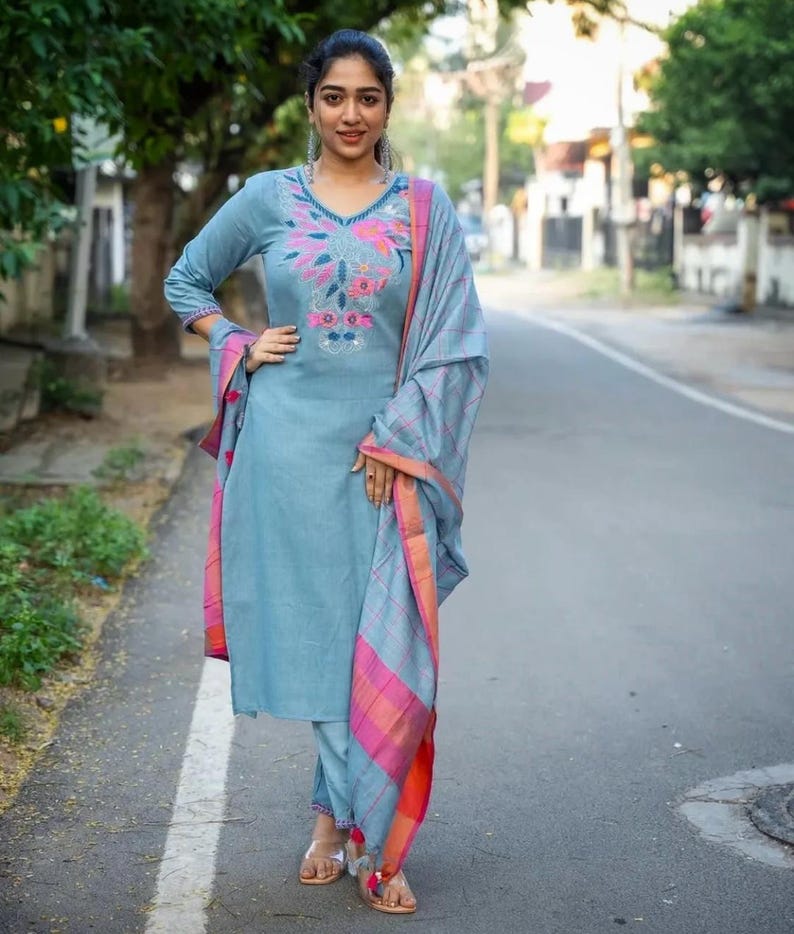 Peut inclure: Une femme portant un salwar kameez bleu clair avec des broderies florales et un dupatta assorti. Le dupatta a une bordure rose et orange.