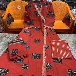 May include: A red wrap dress and matching fabric pieces with a repeating black elephant pattern. The dress has long sleeves and a decorative trim. The fabric pieces include a folded square and a rectangular piece with white polka dots.