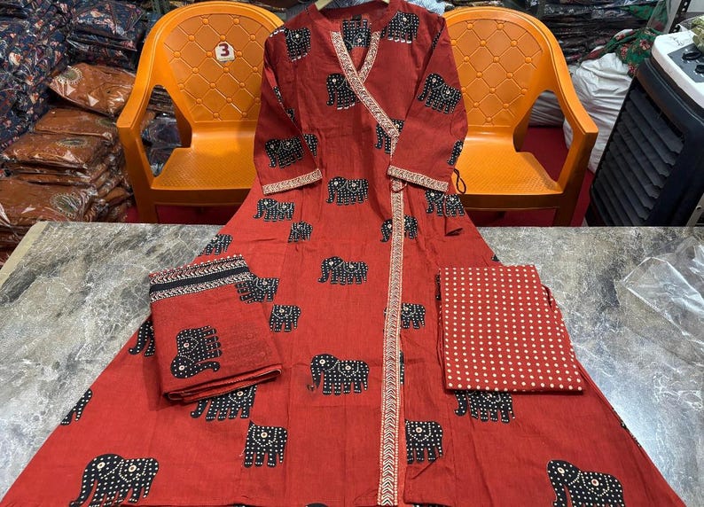 May include: A red wrap dress and matching fabric pieces with a repeating black elephant pattern. The dress has long sleeves and a decorative trim. The fabric pieces include a folded square and a rectangular piece with white polka dots.