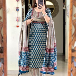 May include: A teal blue and white printed kurta with a matching palazzo pant and dupatta. The kurta has a maroon and white striped neckline and a maroon border. The dupatta has a maroon and white striped border.