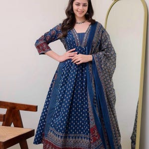 K&ouml;nnte beinhalten: Ein langes, flie&szlig;endes blaues Kleid mit passendem Schal. Das Kleid hat ein detailliertes Muster in Wei&szlig; und Rot, mit einem V-Ausschnitt und Dreiviertel&auml;rmeln. Der Schal drapiert sich &uuml;ber die Schultern und erg&auml;nzt das Design des Kleides. Das Kleid ist f&uuml;r besondere Anl&auml;sse geeignet.