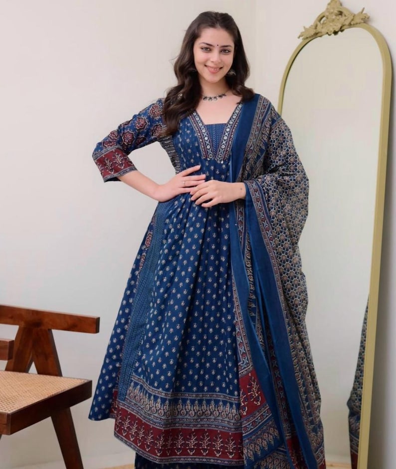 K&ouml;nnte beinhalten: Ein langes, flie&szlig;endes blaues Kleid mit passendem Schal. Das Kleid hat ein detailliertes Muster in Wei&szlig; und Rot, mit einem V-Ausschnitt und Dreiviertel&auml;rmeln. Der Schal drapiert sich &uuml;ber die Schultern und erg&auml;nzt das Design des Kleides. Das Kleid ist f&uuml;r besondere Anl&auml;sse geeignet.