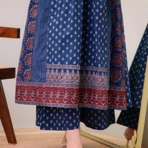 K&ouml;nnte beinhalten: Ein blau gemusterter Rock und eine passende Hose mit dekorativem Rand. Der Rock und die Hose haben ein sich wiederholendes Blumenmuster in Wei&szlig; und Rot. Das Outfit wird mit beigen Sandalen kombiniert.