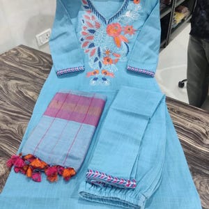 Peut inclure: Une kurta en coton bleu clair avec des broderies florales, un pantalon assorti et une dupatta ray&eacute;e bleu clair et rose avec des pompons orange.