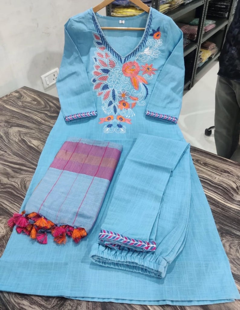 Peut inclure: Une kurta en coton bleu clair avec des broderies florales, un pantalon assorti et une dupatta ray&eacute;e bleu clair et rose avec des pompons orange.