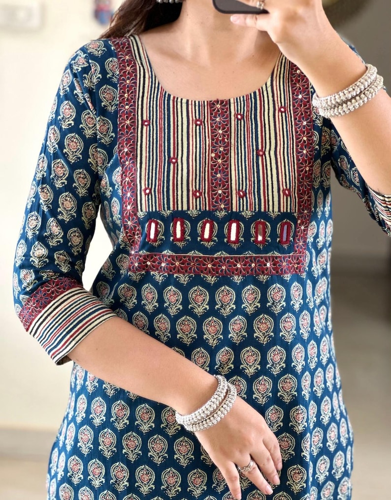 May include: A teal blue cotton kurta with a maroon and white striped neckline and a floral print. The kurta has a maroon border with silver embellishments.
