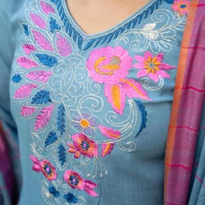 Peut inclure: Une kurta en coton bleu clair avec un motif de broderie florale en rose, bleu et orange. La broderie pr&eacute;sente des d&eacute;tails complexes et un motif paisley.