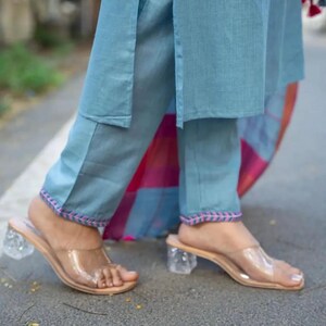 Peut inclure: Un pantalon bleu clair avec des broderies roses et bleues sur les ourlets. Le pantalon est associ&eacute; &agrave; des sandales &agrave; talons en plastique transparent.