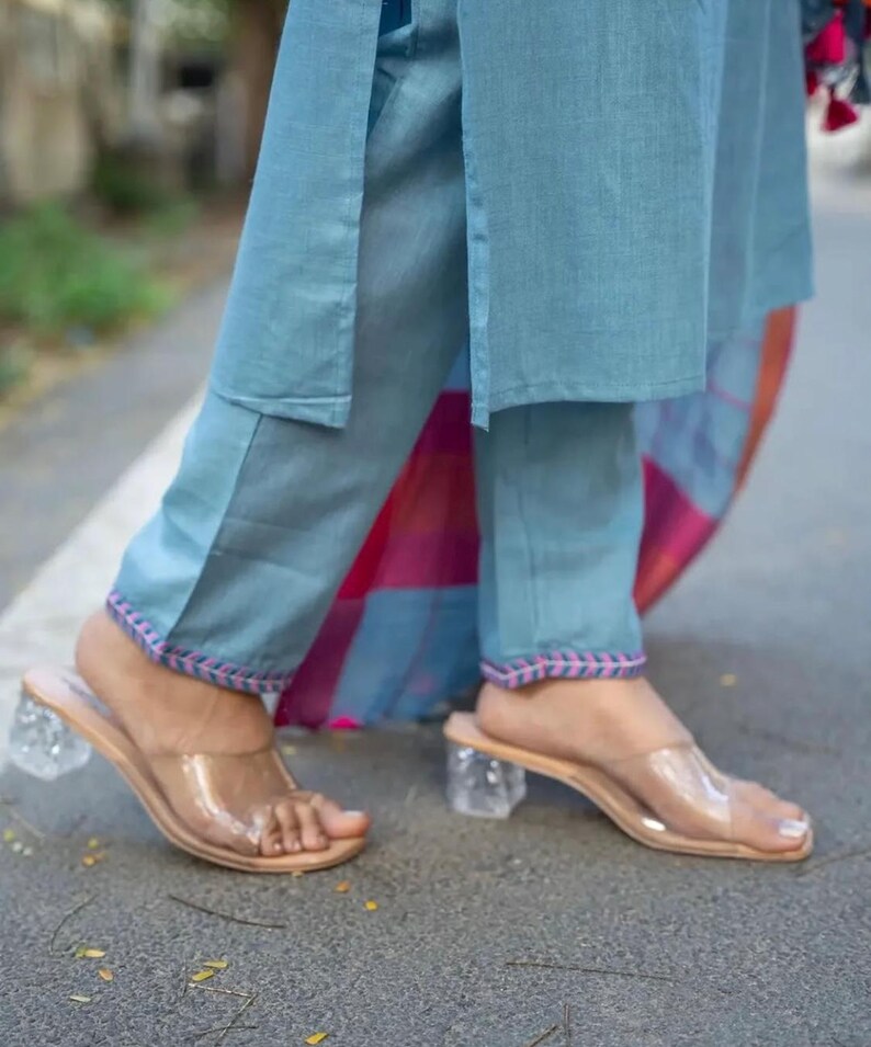 Peut inclure: Un pantalon bleu clair avec des broderies roses et bleues sur les ourlets. Le pantalon est associ&eacute; &agrave; des sandales &agrave; talons en plastique transparent.
