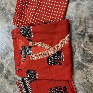 May include: A red pajama set with a top, pants, and a scarf. The top and scarf feature a black elephant pattern with white polka dots. The pants are red with white polka dots. The set is made of a lightweight fabric.