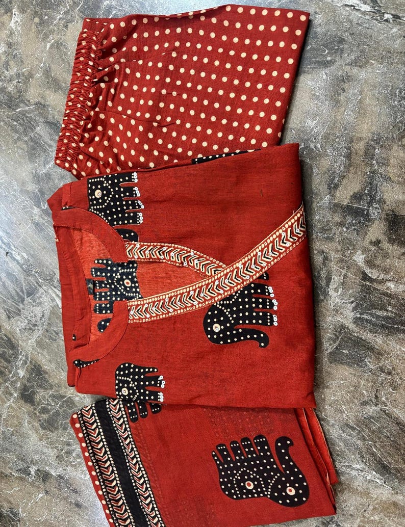 May include: A red pajama set with a top, pants, and a scarf. The top and scarf feature a black elephant pattern with white polka dots. The pants are red with white polka dots. The set is made of a lightweight fabric.
