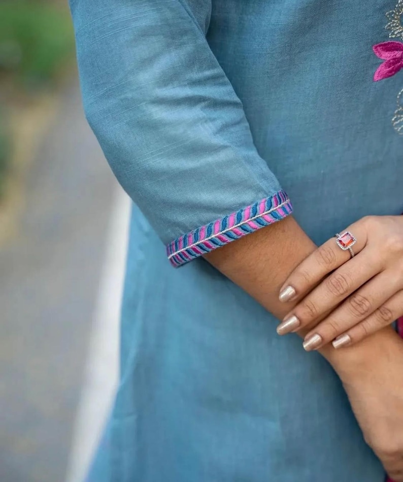 Peut inclure: Une tunique en coton bleu clair avec des bordures brod&eacute;es roses et bleues sur les manches. La tunique a un effet ombr&eacute; subtil.