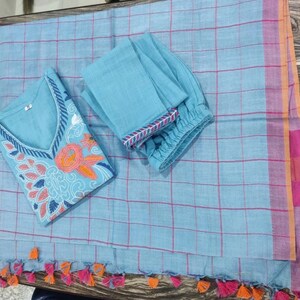 Peut inclure: Un ensemble salwar kameez en coton bleu clair avec des d&eacute;tails floraux brod&eacute;s. L'ensemble comprend un haut &agrave; manches longues, un pantalon et une dupatta assortie &agrave; motif &agrave; carreaux et des glands roses et orange.