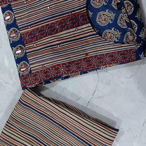 May include: A two-piece clothing set featuring a striped top with a floral border and a matching striped bottom. The top has a round neckline and is decorated with small, shiny embellishments. The fabric is a light brown with blue, red, and black stripes.
