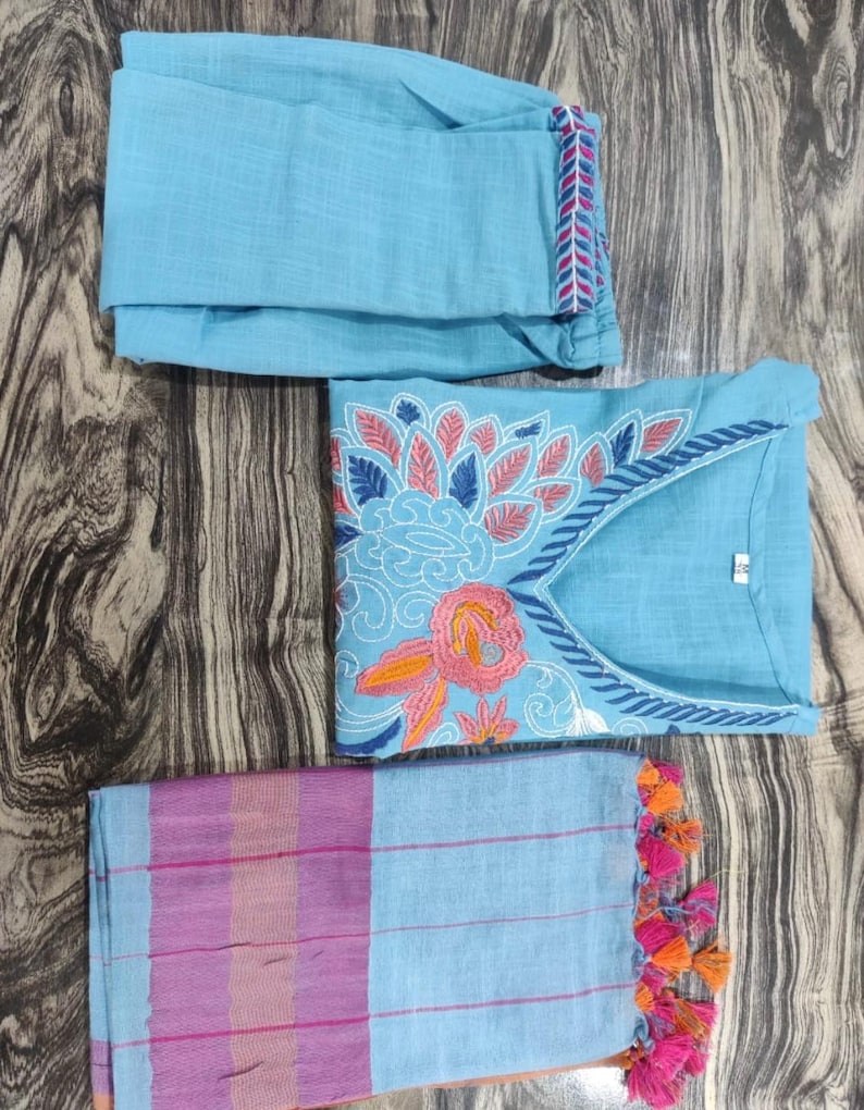 Peut inclure: Un ensemble de v&ecirc;tements trois pi&egrave;ces bleu clair avec des broderies florales. L'ensemble comprend un haut &agrave; manches longues, un pantalon et une &eacute;charpe assortie avec des glands.