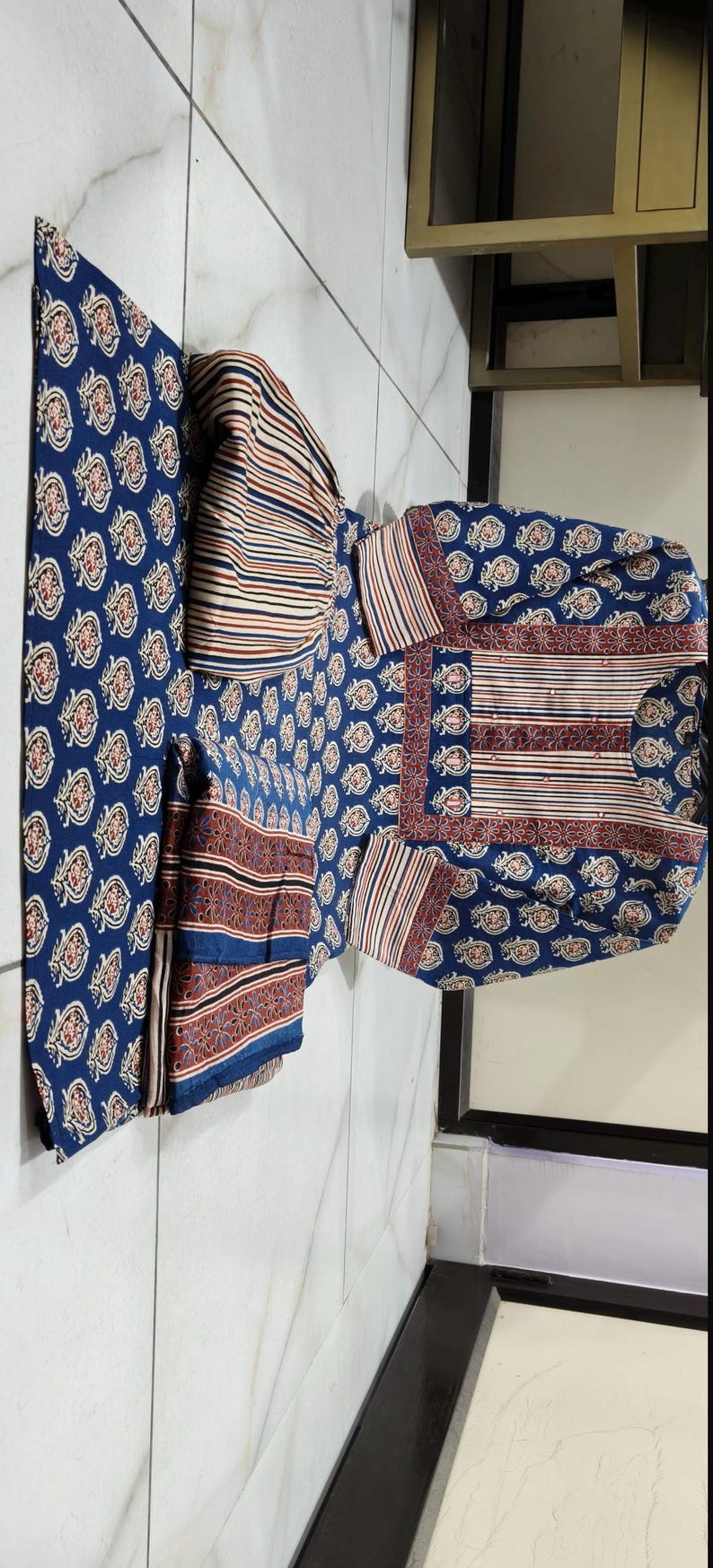 May include: A set of three blue and white patterned fabric squares. The fabric has a paisley design with red and white accents. The squares are folded and arranged on a white tiled floor.