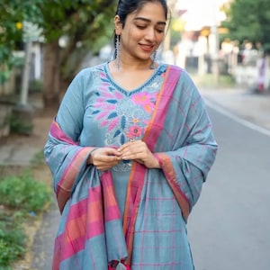 Peut inclure: Une femme portant une kurta &agrave; carreaux bleus et roses avec des broderies florales. La kurta a un col en V et des manches longues. Elle porte un dupatta assorti avec une bordure rose et orange.