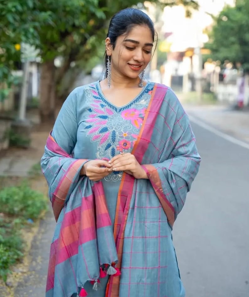 Peut inclure: Une femme portant une kurta &agrave; carreaux bleus et roses avec des broderies florales. La kurta a un col en V et des manches longues. Elle porte un dupatta assorti avec une bordure rose et orange.