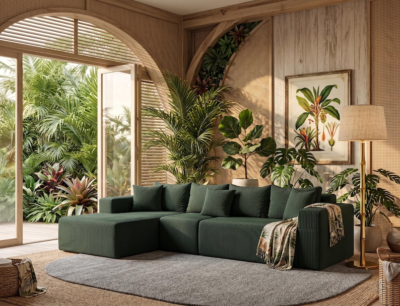 May include: A dark green sectional sofa with several matching throw pillows. The sofa is in a room with a large window overlooking a lush garden. A botanical print and a floor lamp are also visible.