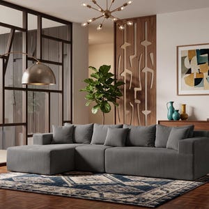May include: A modern living room featuring a gray sectional sofa with matching throw pillows. A patterned rug in blue and cream tones sits on a hardwood floor. A gold arched floor lamp and abstract art complete the space.