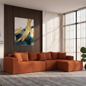 May include: An orange sectional sofa with multiple cushions is the focal point of a modern living room. A large abstract painting hangs on a dark wood-paneled wall. A floor lamp and a potted plant add to the decor.