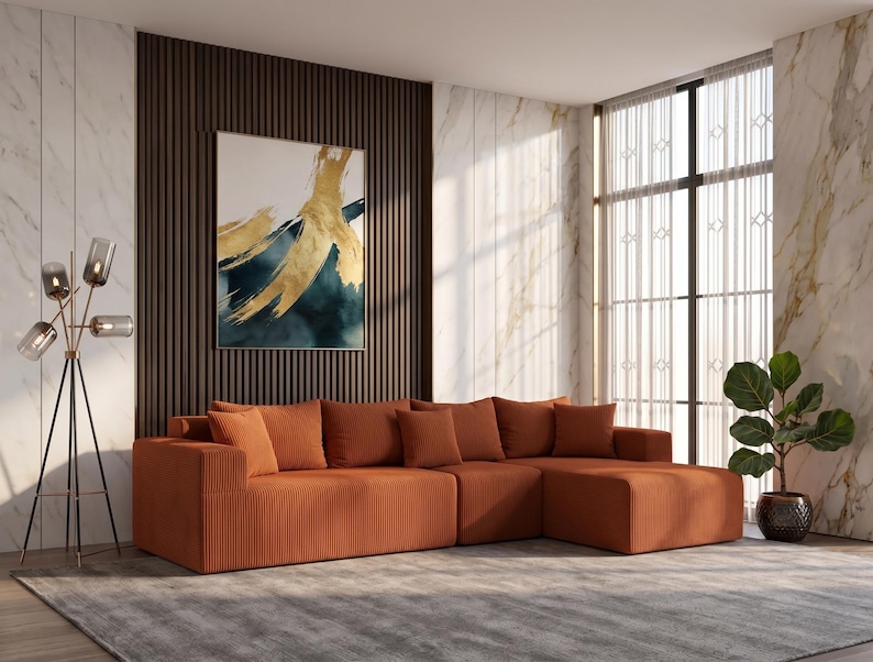 May include: An orange sectional sofa with multiple cushions is the focal point of a modern living room. A large abstract painting hangs on a dark wood-paneled wall. A floor lamp and a potted plant add to the decor.