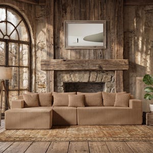 May include: A modern, modular sectional sofa in a neutral beige corduroy fabric. The sofa is arranged in an L-shape and includes several matching throw pillows. The room features a rustic aesthetic with a large window, wooden floors, and a stone fireplace.