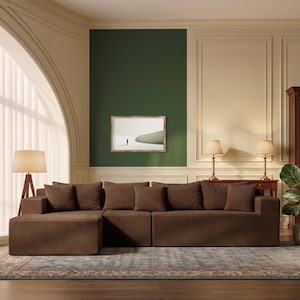 May include: A brown corduroy sectional sofa with multiple cushions. The sofa is placed on a patterned rug in a room with a green accent wall and a framed picture. A wooden bookcase and a potted plant are also visible.