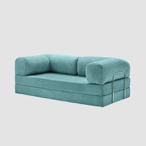 May include: A teal corduroy sofa with rounded armrests and a rectangular seat. The sofa has a modular design, with a folded base and a metal frame on the armrest. The corduroy fabric has a ribbed texture.