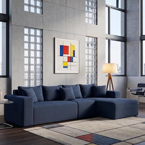 May include: A modern living room featuring a large, navy blue sectional sofa with several matching throw pillows. A framed abstract art piece hangs on the concrete wall. A glass side table and a wooden floor lamp are also present.