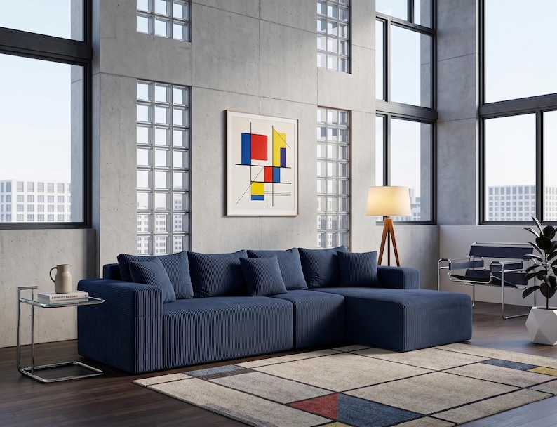 May include: A modern living room featuring a large, navy blue sectional sofa with several matching throw pillows. A framed abstract art piece hangs on the concrete wall. A glass side table and a wooden floor lamp are also present.
