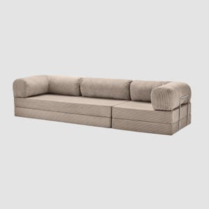 May include: A modular beige corduroy sofa with rounded armrests and back cushions. The sofa is composed of several sections, offering a customizable seating arrangement. The design features a minimalist aesthetic with a neutral color palette.