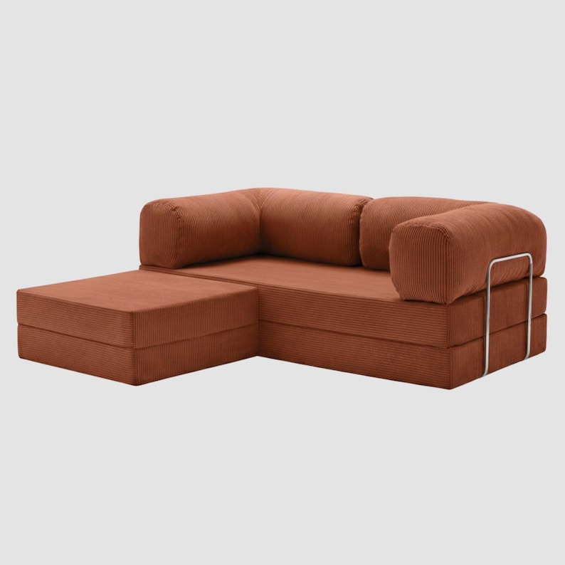 May include: A modular, rust-colored corduroy sectional sofa with a chaise lounge. The sofa features a low profile, rounded armrests, and a metal frame detail. The fabric has a ribbed texture, and the design is modern and minimalist.