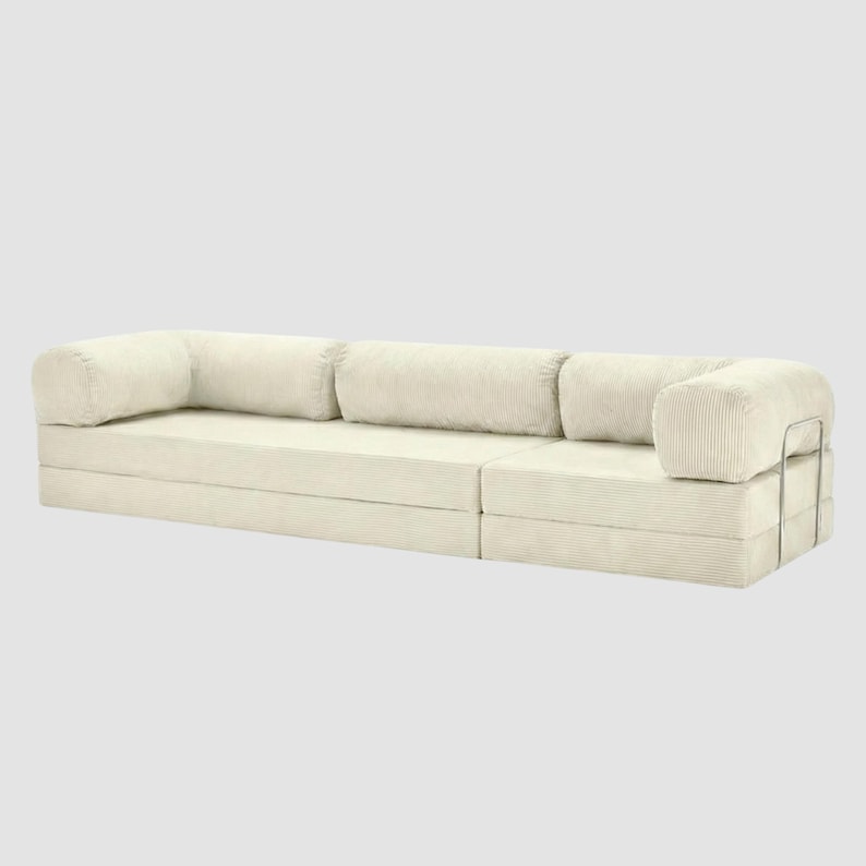 May include: A modular, cream-colored corduroy sofa with a minimalist design. The sofa features a low profile, with a series of rectangular cushions and armrests. The armrests are supported by a silver metal frame. The sofa is designed for comfort and modern living.