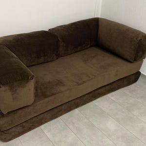 May include: A brown corduroy sofa with a low profile and rounded armrests. The sofa has a rectangular seat and back cushions. The frame appears to be metal. The sofa is placed against a white wall.