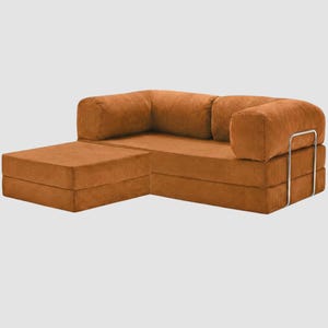 Puede incluir: Un sof&aacute; seccional modular de pana en un tono naranja c&aacute;lido. El sof&aacute; cuenta con una chaise longue y un reposabrazos redondeado con un marco de metal plateado. La tela de pana tiene una textura acanalada, y el dise&ntilde;o es moderno y minimalista.