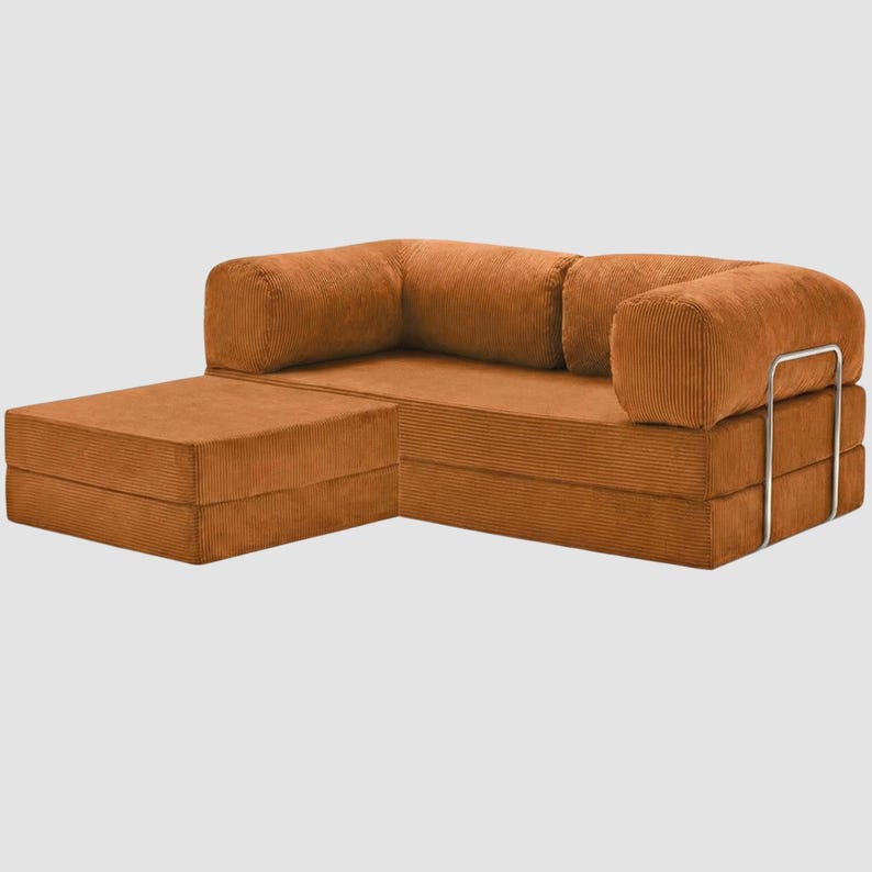 Puede incluir: Un sof&aacute; seccional modular de pana en un tono naranja c&aacute;lido. El sof&aacute; cuenta con una chaise longue y un reposabrazos redondeado con un marco de metal plateado. La tela de pana tiene una textura acanalada, y el dise&ntilde;o es moderno y minimalista.