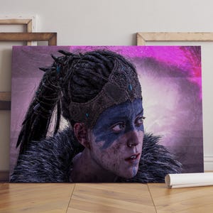 Puede incluir: Una impresión en lienzo que presenta un retrato de una persona con cabello oscuro y pintura facial azul. La persona lleva un tocado decorativo y una prenda forrada de piel. El fondo es una mezcla de morado y blanco.