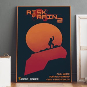 May include: A framed poster with the text "RISK of RAIN 2" above a large orange sun. A silhouette of a person stands on a red rock formation, holding up a device. The poster also includes the text "HOPPO GAMES" and the names of the game developers.
