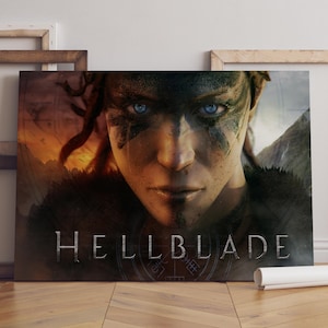 May include: A canvas print featuring the game title "Hellblade." The artwork showcases a close-up of a person with striking blue eyes and face paint. The background has a dark, dramatic landscape.