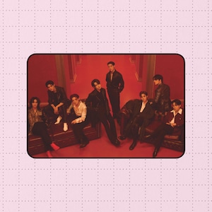 Könnte beinhalten: Eine Studiogruppe von neun Personen in verschiedenen Outfits. Der Hintergrund ist tiefrot, und die Personen sitzen auf einem braunen Ledersofa. Die Beleuchtung ist dramatisch und erzeugt Schatten und Glanzlichter auf ihrer Kleidung.