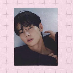 May include: A portrait of a person with dark hair and a dark sweater. The person is looking towards the camera with a slight smile. The background is a light grey colour.