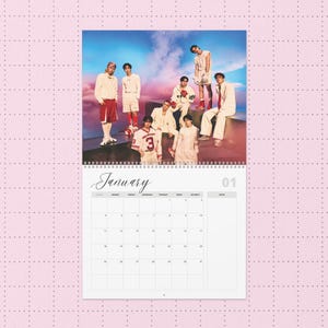 Peut inclure: Calendrier à spirale avec une photo d'un groupe de personnes devant un ciel coloré. Le calendrier est ouvert sur le mois de janvier, avec le mot "Janvier" écrit en cursive. La date "01" est visible.