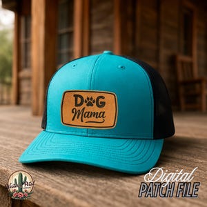 May include: A turquoise and black trucker hat with a brown leather patch that says "Dog Mama" with a paw print.