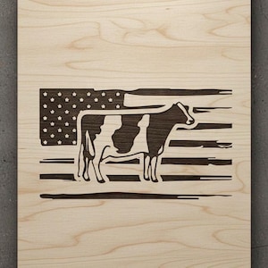 May include: Wooden sign featuring a cow silhouette integrated into an American flag design. The flag's stars and stripes are visible, with the cow's form replacing a portion of the flag. The sign is made of light-colored wood.