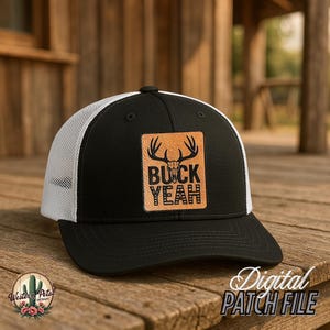 Pode incluir: Boné de caminhoneiro preto e branco com um remendo de couro marrom que diz "Buck Yeah" com um gráfico de crânio de veado.