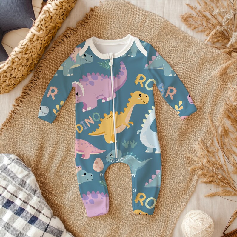 May include: A teal baby onesie with a white collar and a full-length zipper. The onesie features a colorful dinosaur pattern with the words "ROAR" and "DINO". The dinosaurs are in shades of pink, yellow, and blue.