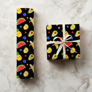 May include: Black wrapping paper and a wrapped gift box feature a repeating pattern of smiling fruit illustrations. The design includes watermelons, pineapples, lemons, avocados, bananas, blueberries, and stars. The gift box is tied with a white ribbon.